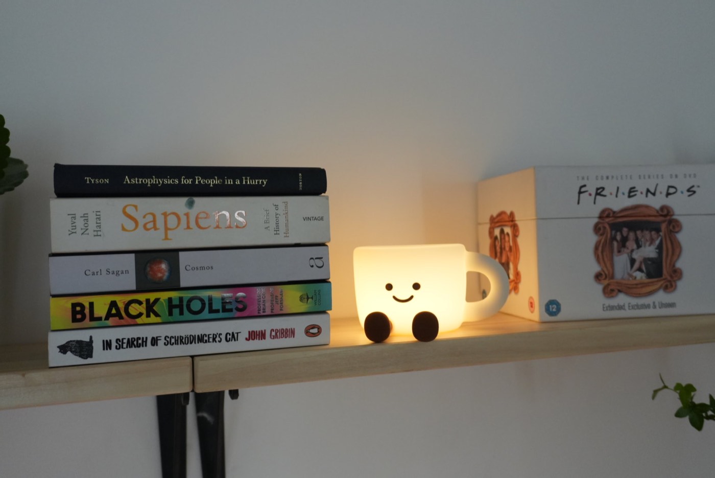 Smiling coffee-shaped lamp glowing on the shelf beside a stack of books